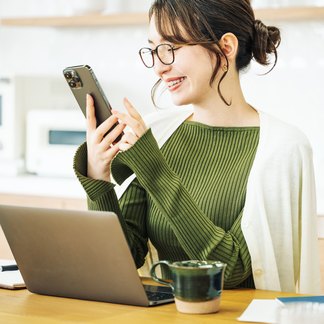 在宅勤務中に自宅のデスクでスマートフォンから社内ラジオを聴く社員