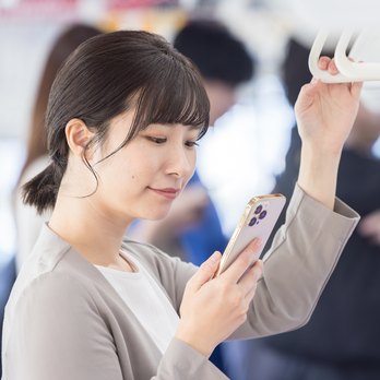 通勤中の電車でスマートフォンから社内ラジオを聴く社員